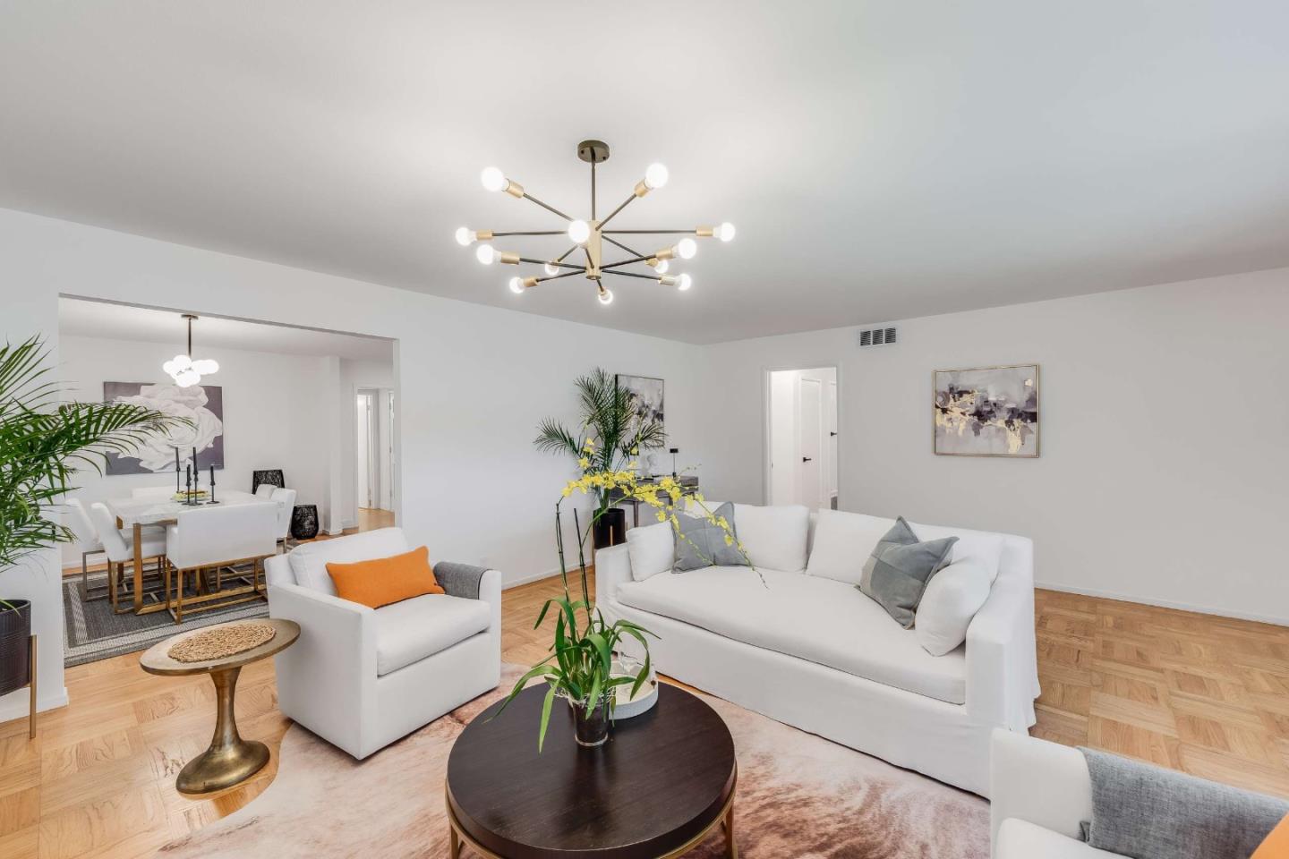 Staged living room with white sofas, parquet floors, and a modern multi-arm chandelier.