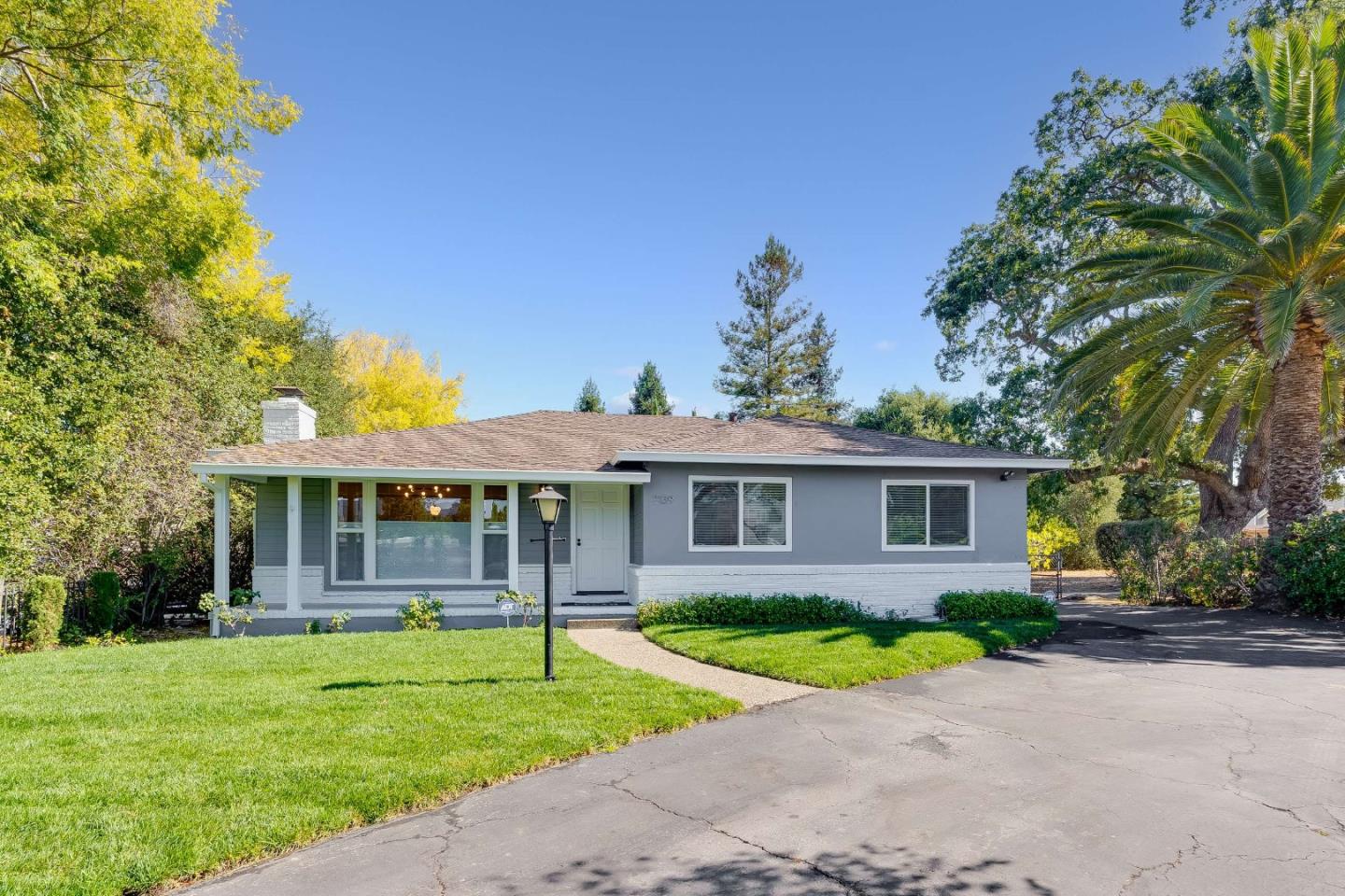 Single-story gray house with large front windows, a green lawn, and a paved driveway.