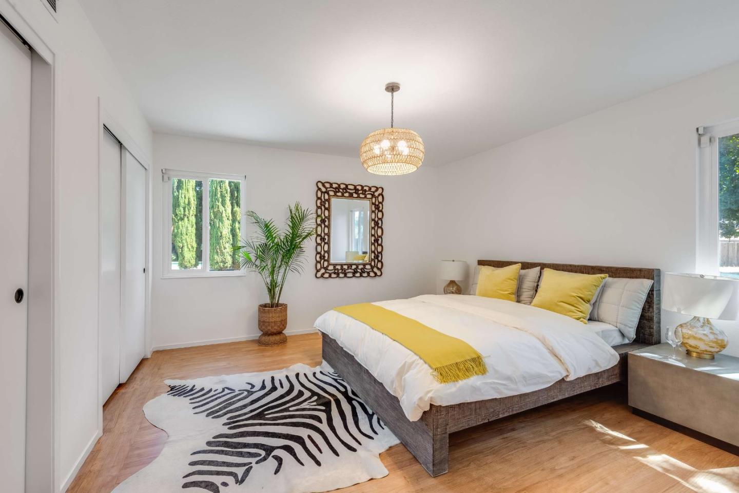 Staged bedroom with yellow-accented white bedding, a zebra-pattern rug, and a potted palm.
