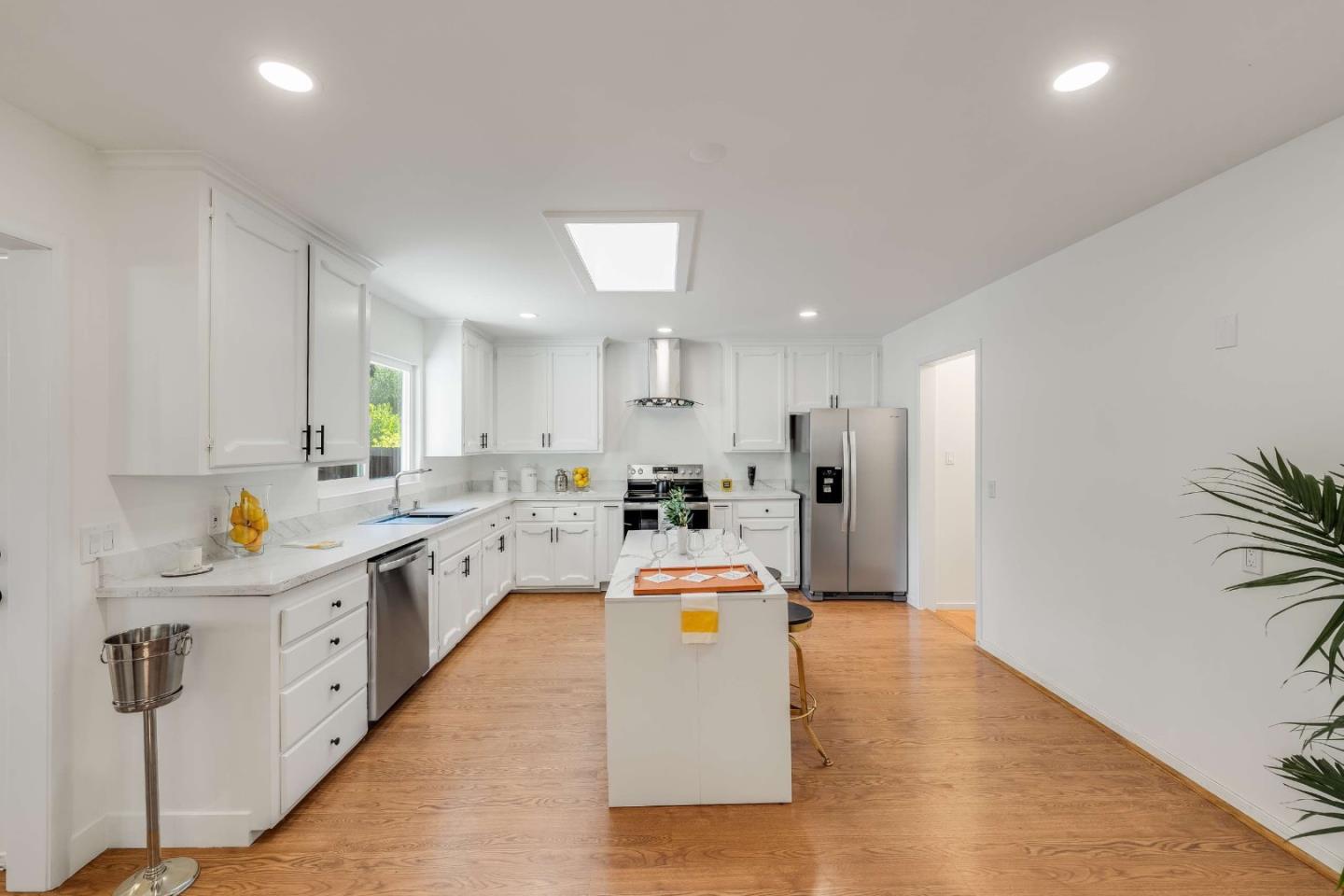 Bright white kitchen with a central island, stainless steel appliances, and warm wood flooring.