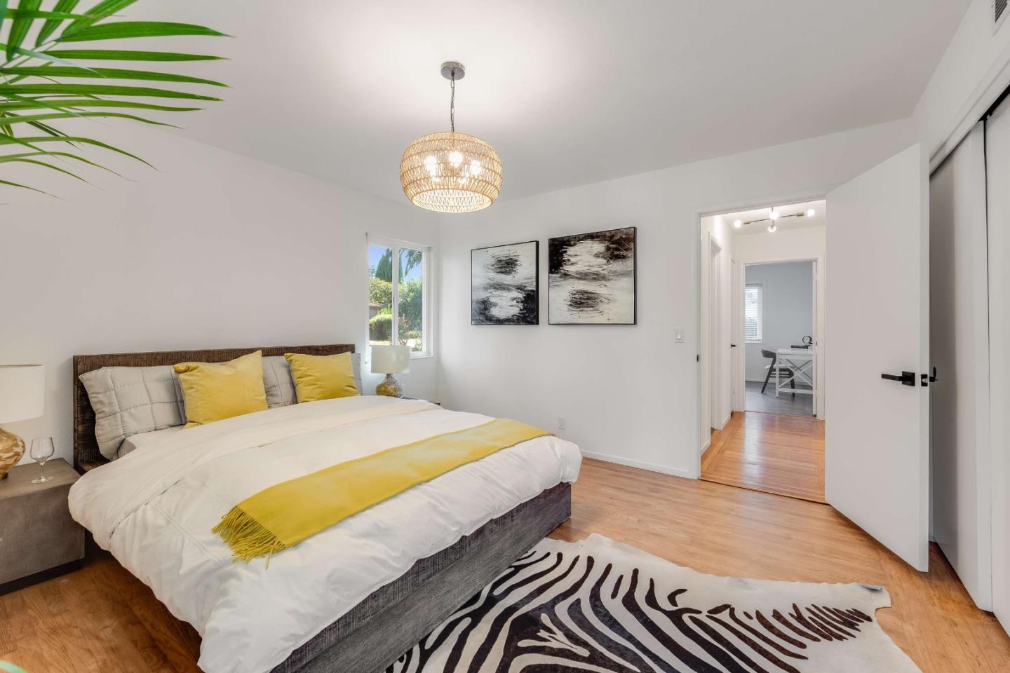 Staged bedroom with white bedding, yellow accents, a woven pendant light, and a black-and-white rug.