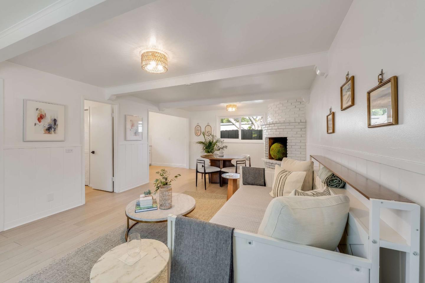 Staged living room with cream seating, pale wood floors, and a white brick fireplace.