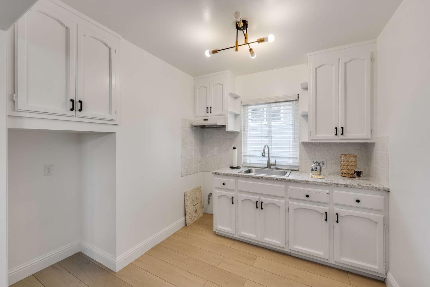 Bright kitchen with white paneled cabinets, a window above the sink, and light wood flooring.