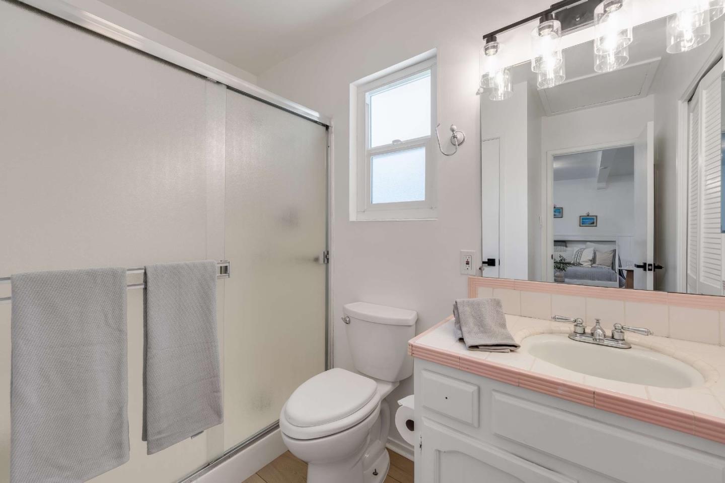 Bathroom with glass shower, gray towels, and white vanity with pink tile trim.