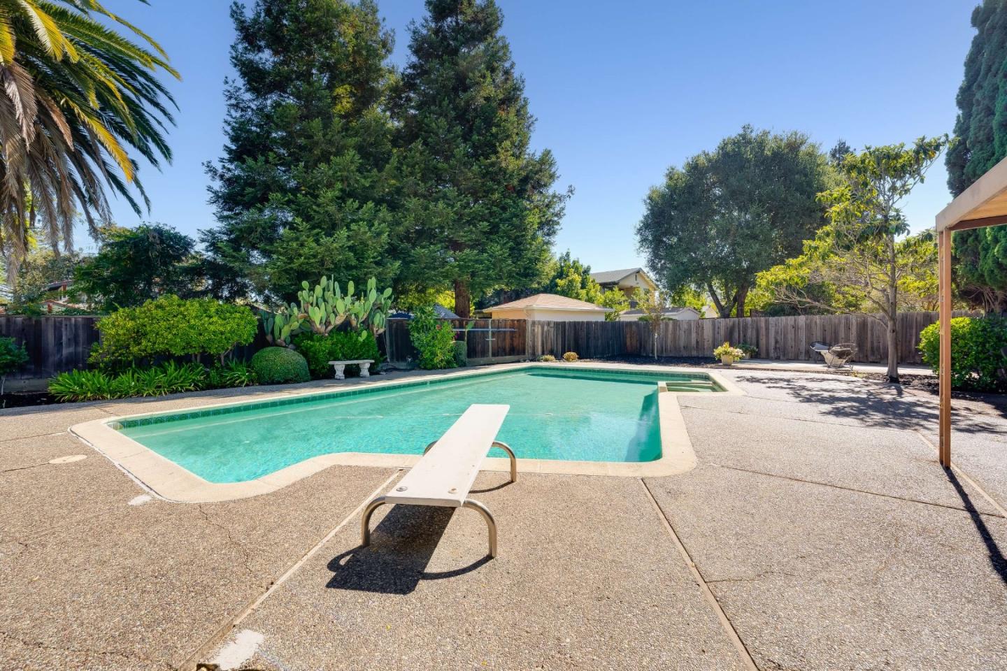 Backyard swimming pool with a diving board and mature trees.