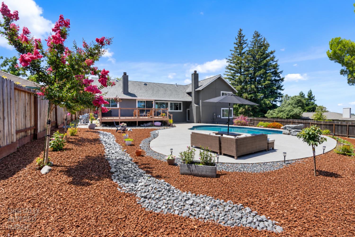 Landscaped backyard with a swimming pool, curved patio, raised deck, and flowering tree.