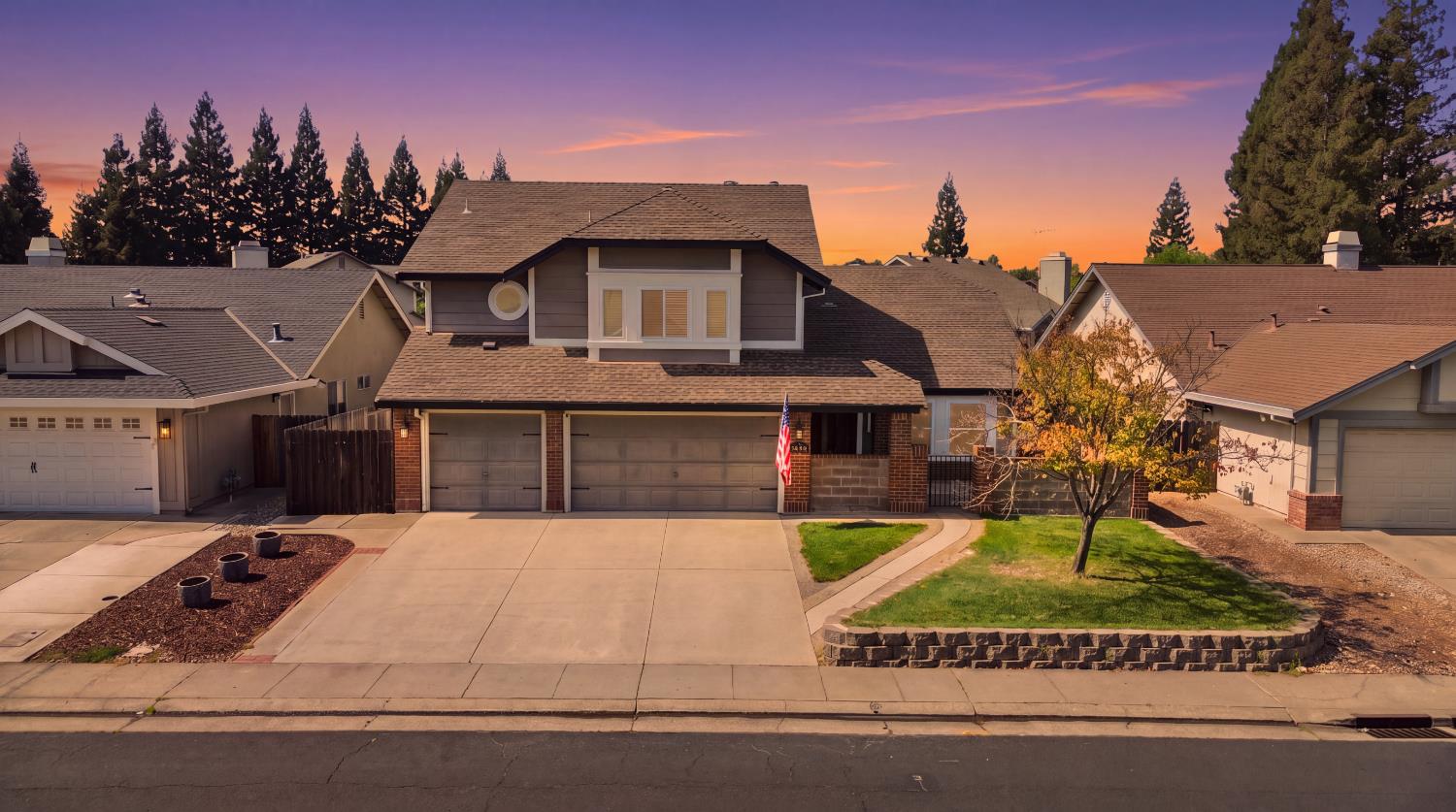Gray two-story home with an attached garage and front lawn beneath a purple-orange dusk sky.