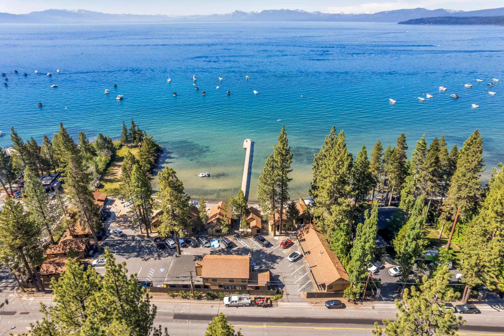 Lakeside property complex with a long dock, boats on the water, and mountains beyond.