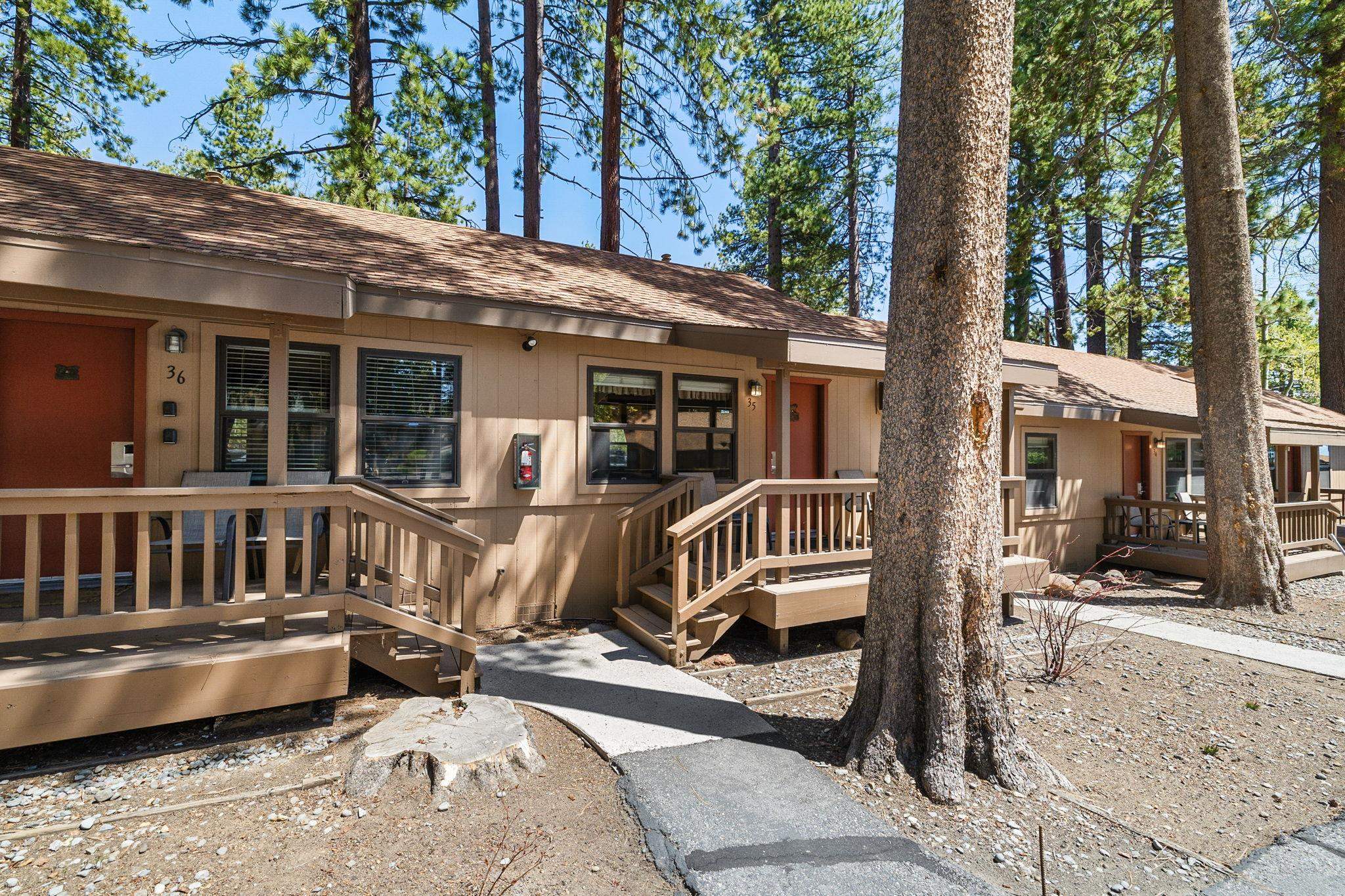 Attached tan homes with wooden decks and stairs among tall pine trees.