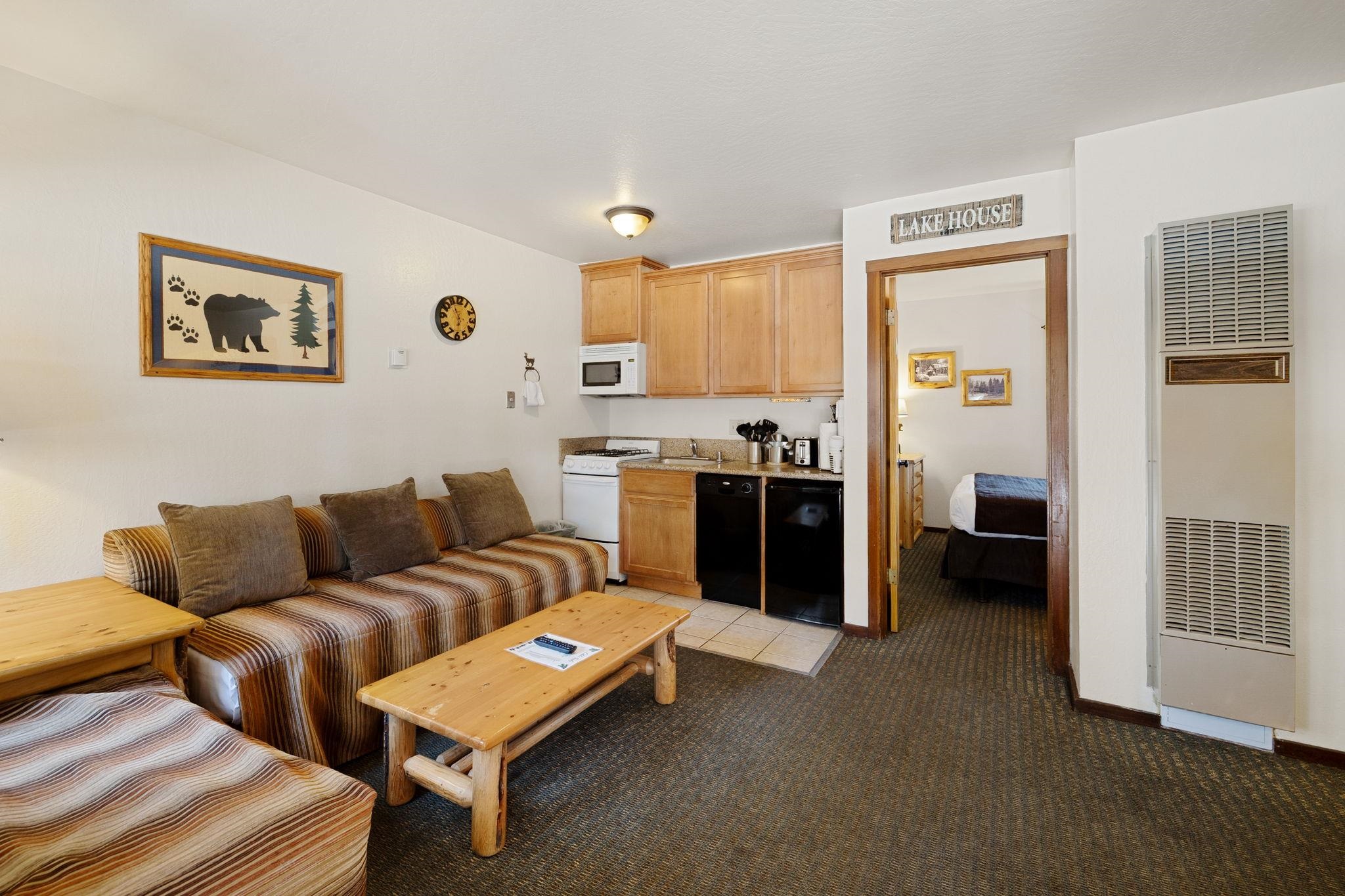 Furnished living area with a striped sofa, compact kitchenette, and bedroom doorway.