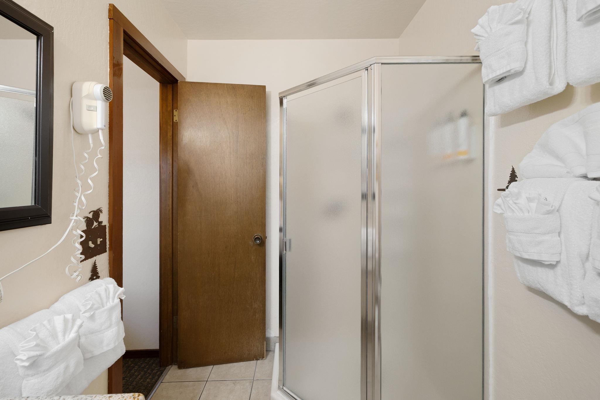 Bathroom with a glass shower enclosure, neatly arranged white towels, and an open wooden door.