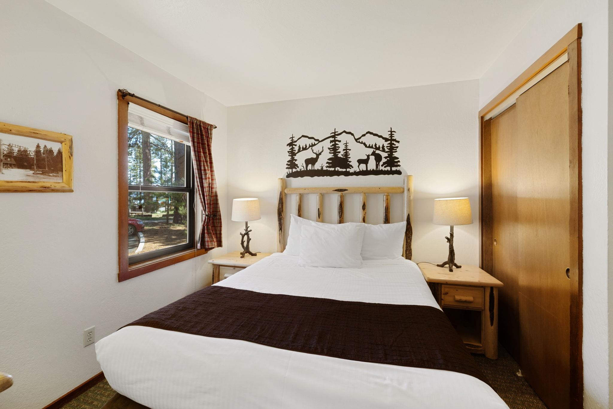 Bedroom with a rustic log headboard, deer-and-mountain wall art, and plaid curtains.