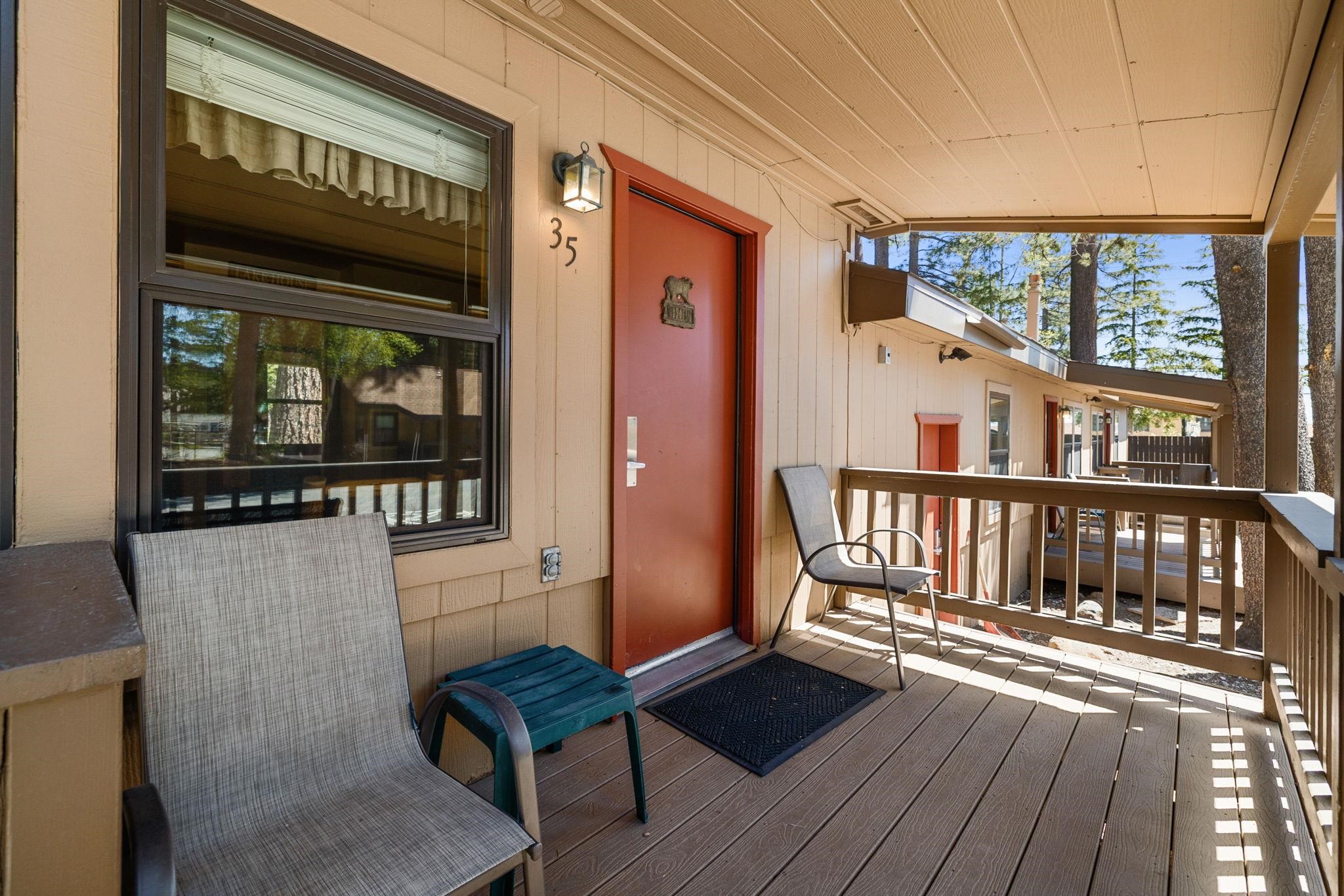 Covered deck outside unit 35, with a red door, two chairs, and a railing overlooking pine trees.