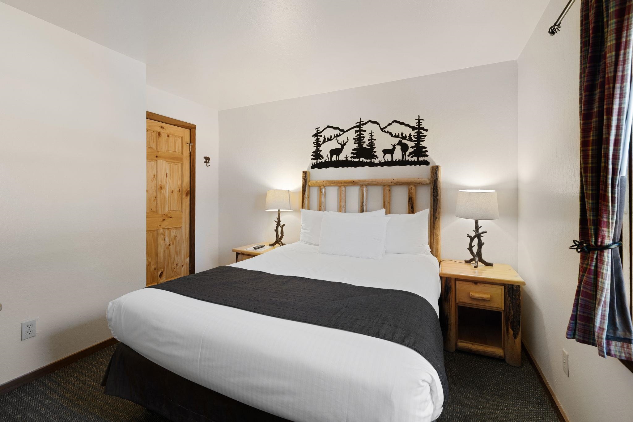 Bedroom with a white bed, rustic log furnishings, and mountain-and-wildlife wall decoration.
