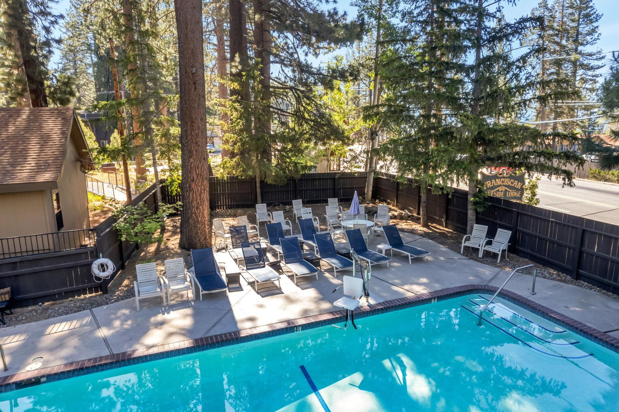 Outdoor pool bordered by lounge chairs and tall evergreens, with a Franciscan Seaside Lodge sign.