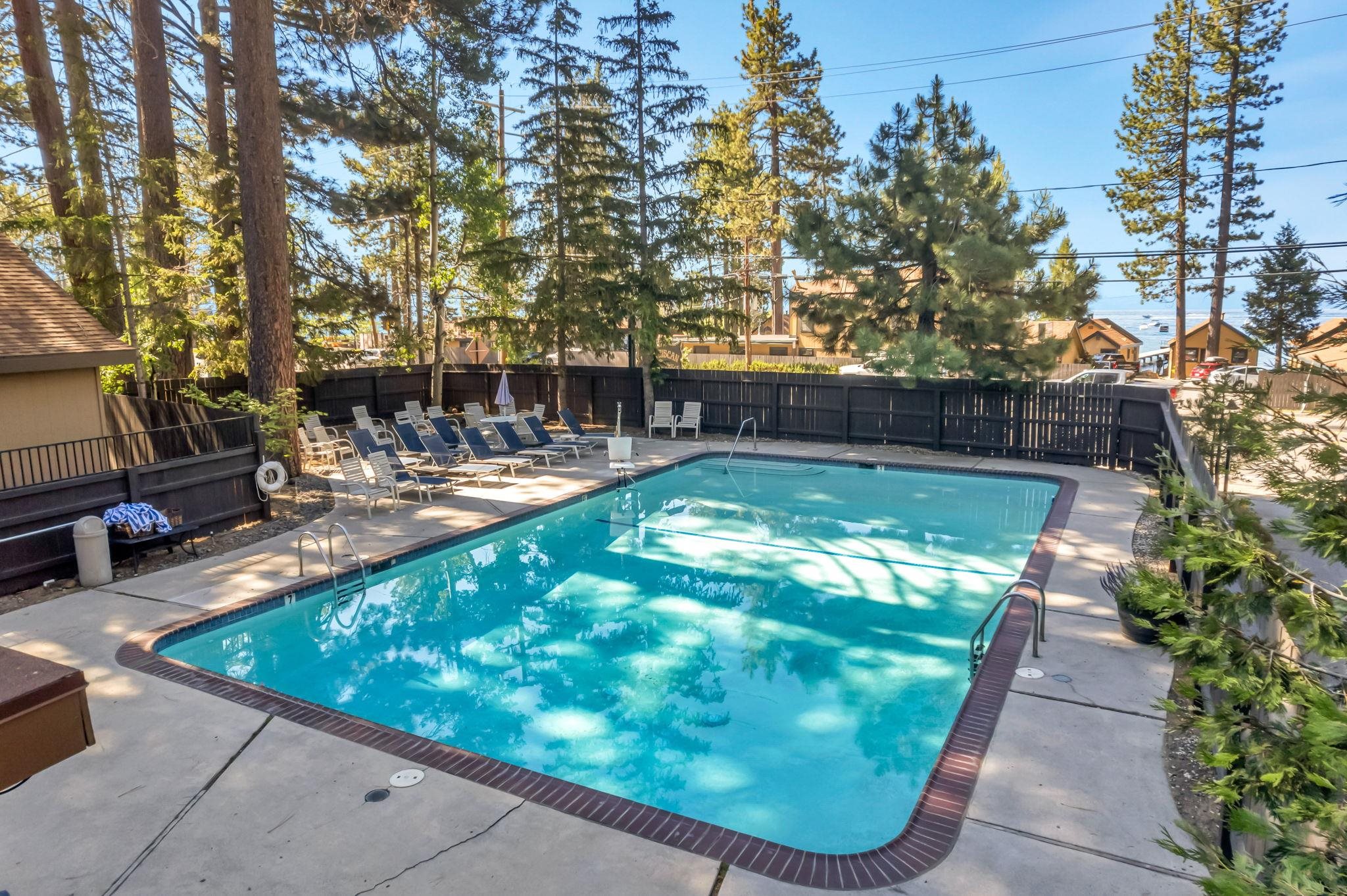 Outdoor pool with lounge chairs, pine trees, and Lake Tahoe visible beyond the fence.