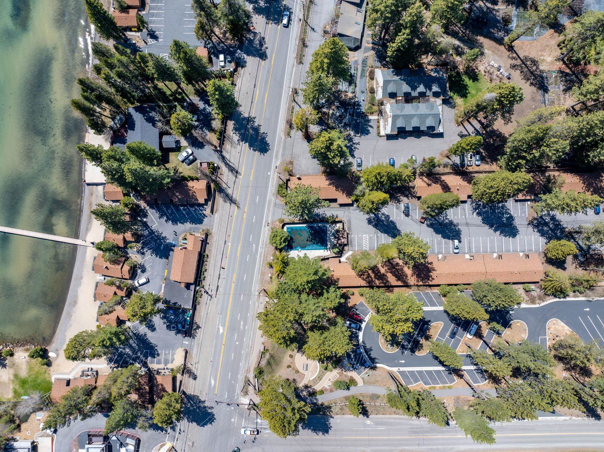 Aerial view of lakeside buildings, parking, and a swimming pool beside the road.