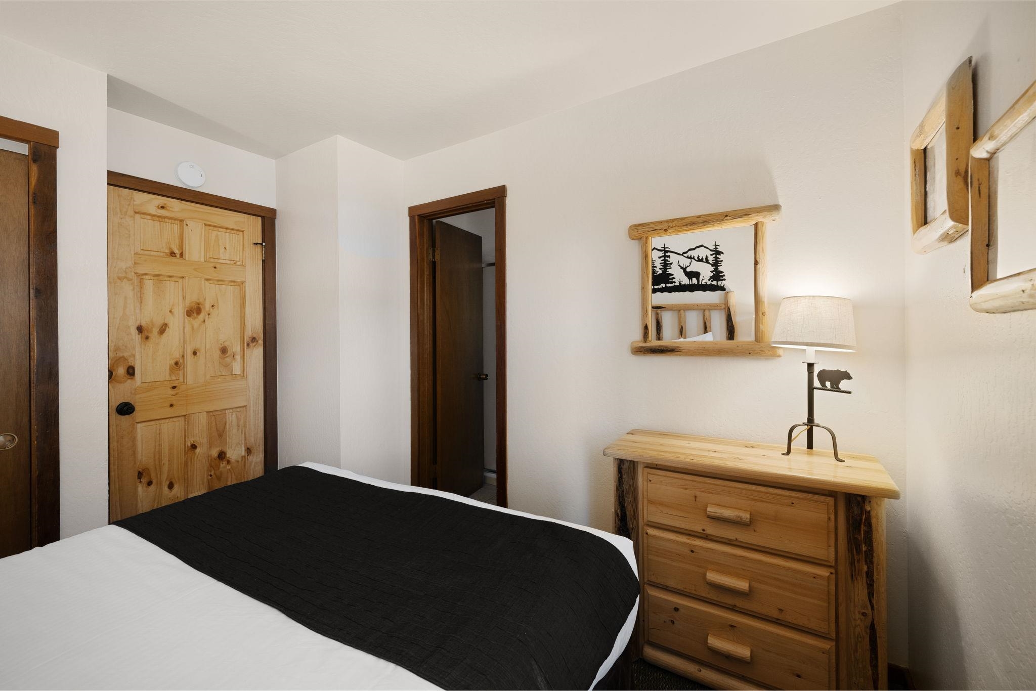 Bedroom with black-and-white bedding, knotty pine doors, and a rustic wooden dresser.