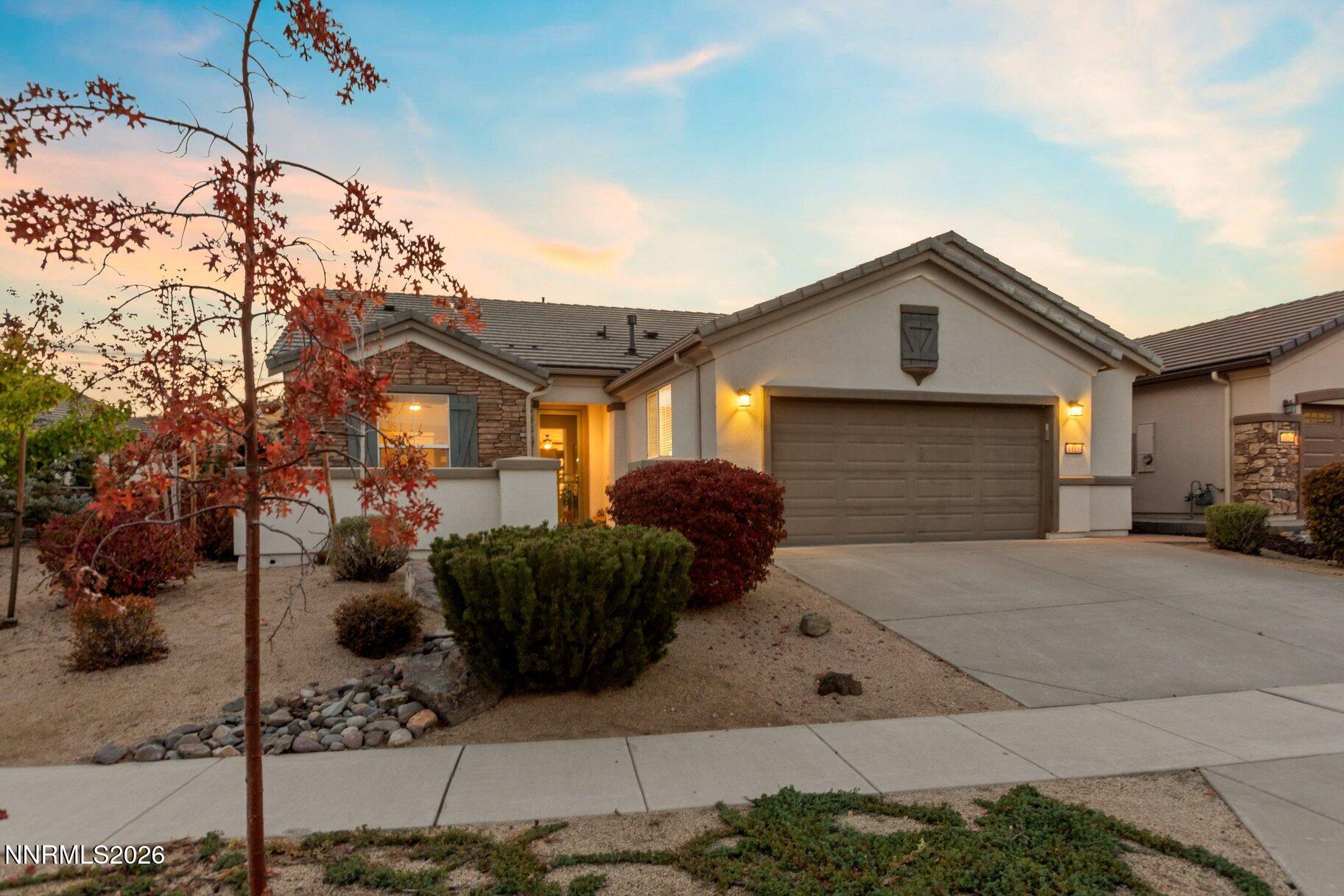 Single-story home with stone accents and a two-car garage, framed by autumn foliage at dusk.