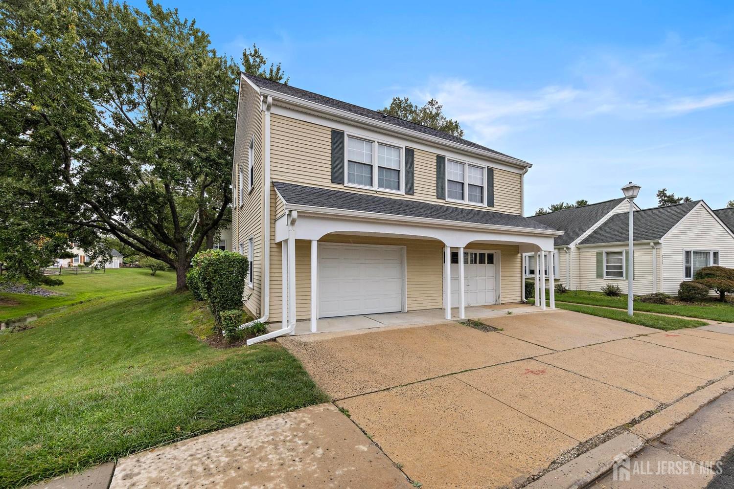 Two-story beige home with a covered porch, attached garage, and wide concrete driveway.