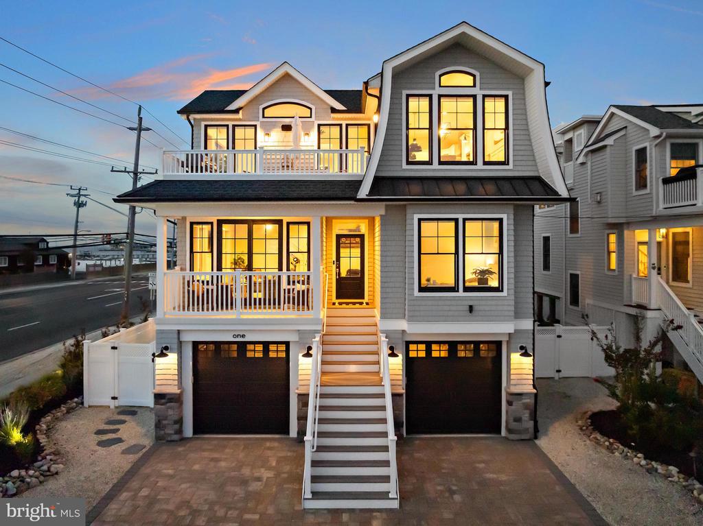 Gray multi-story house at dusk with illuminated windows, white balconies, and a broad central staircase.