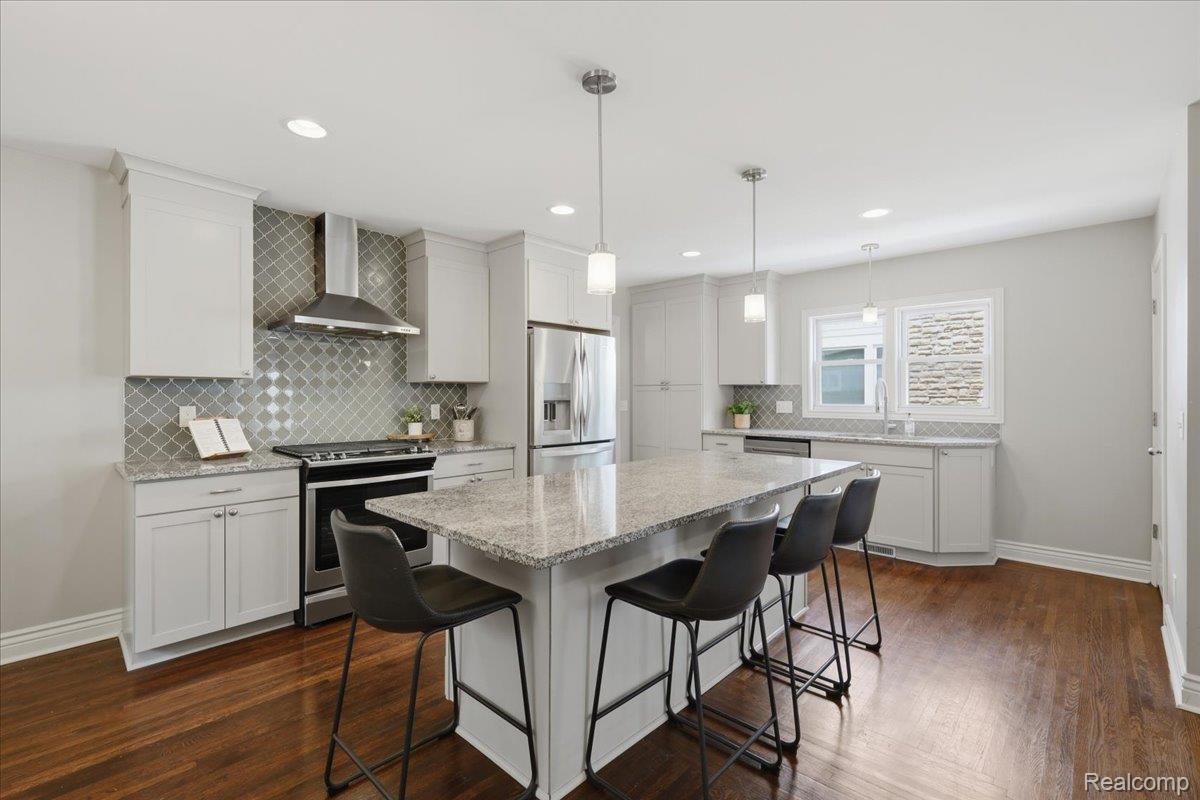 Updated kitchen with white cabinets, patterned tile backsplash, stainless steel appliances, and a granite island with bar stools.