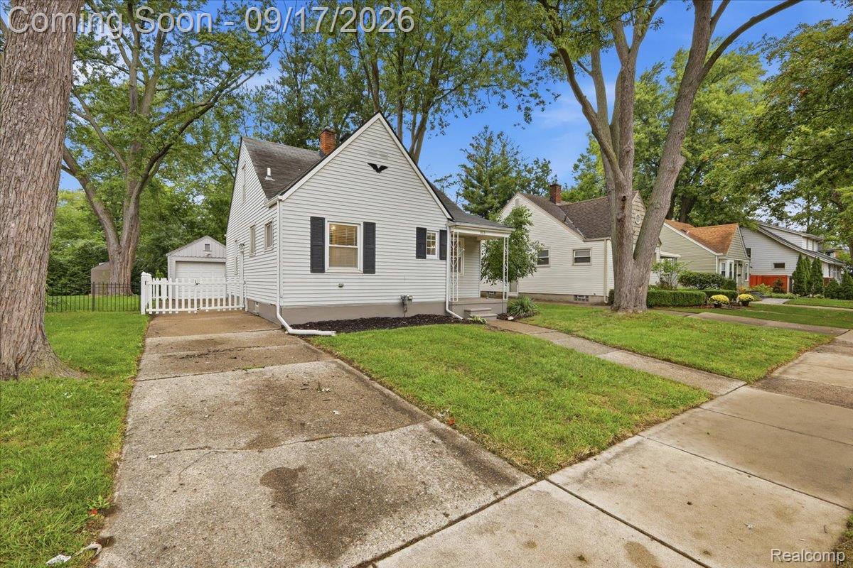White-sided home with black shutters, a covered porch, and a driveway to a detached garage.