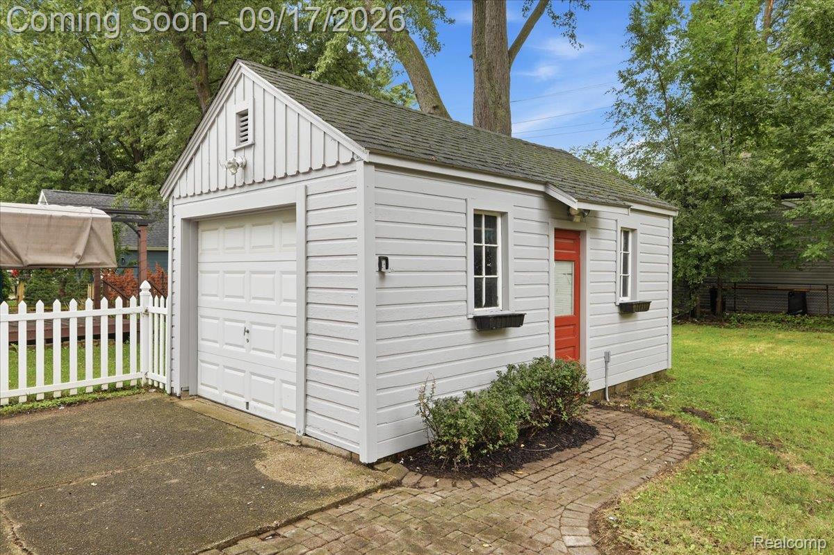 White detached garage with a red side door, beside a paved driveway and brick walkway.