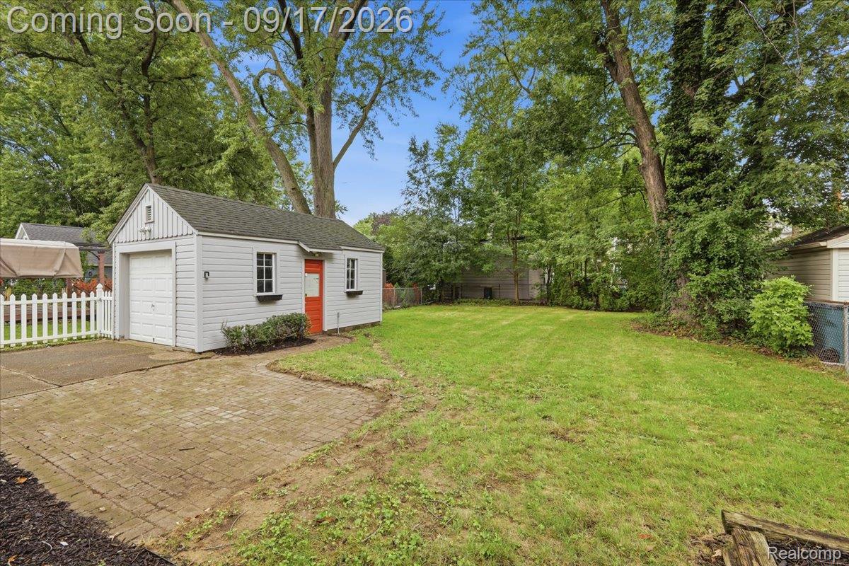 Backyard with a white detached shed, red door, paved patio, lawn, and mature trees.