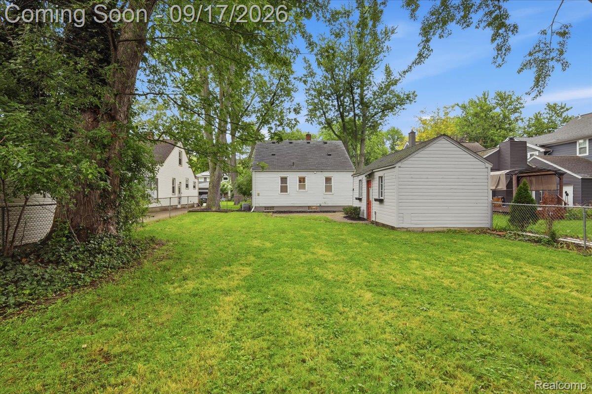 Rear of a light-sided house and detached garage beyond a broad grassy backyard.