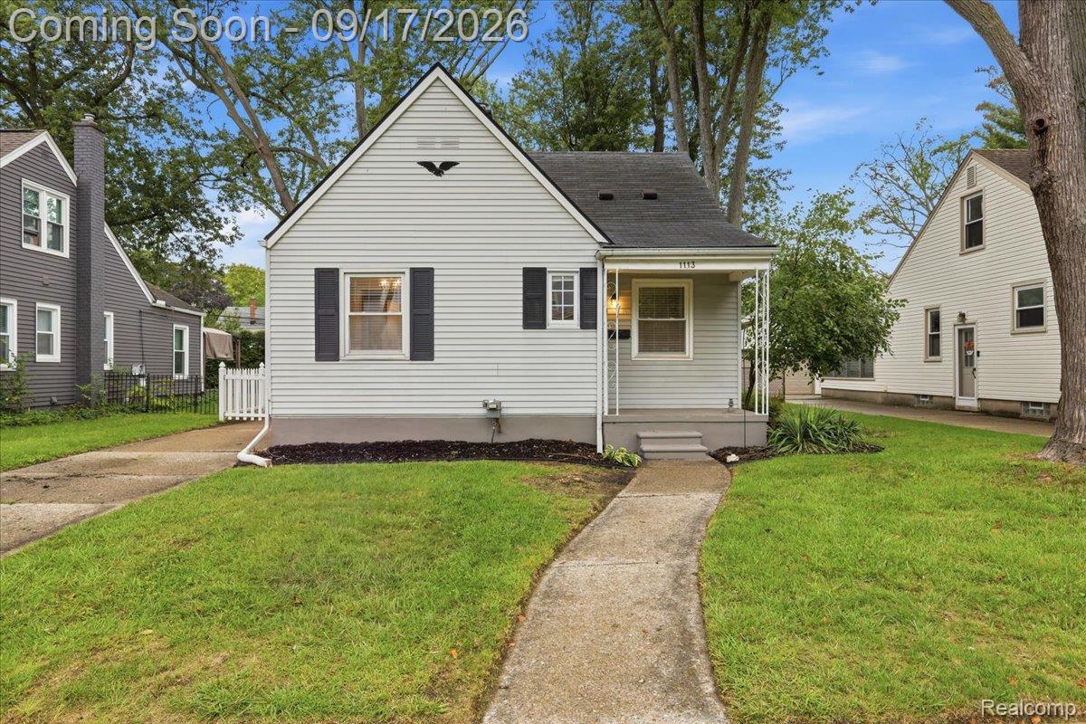 White-sided gable-front house with black shutters, a small covered porch, lawn, and concrete walkway.