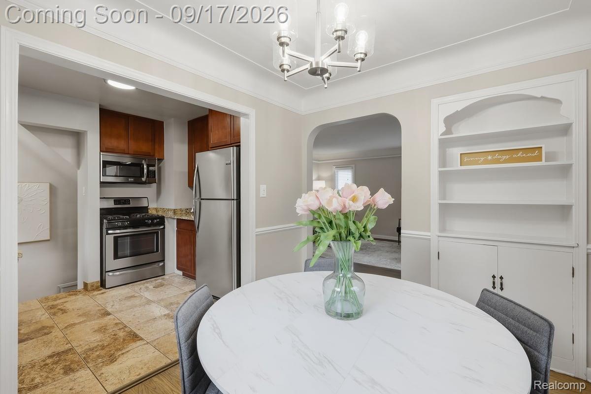 Dining room with a round white table, pink flowers, built-in shelving, and an arched opening to the kitchen.