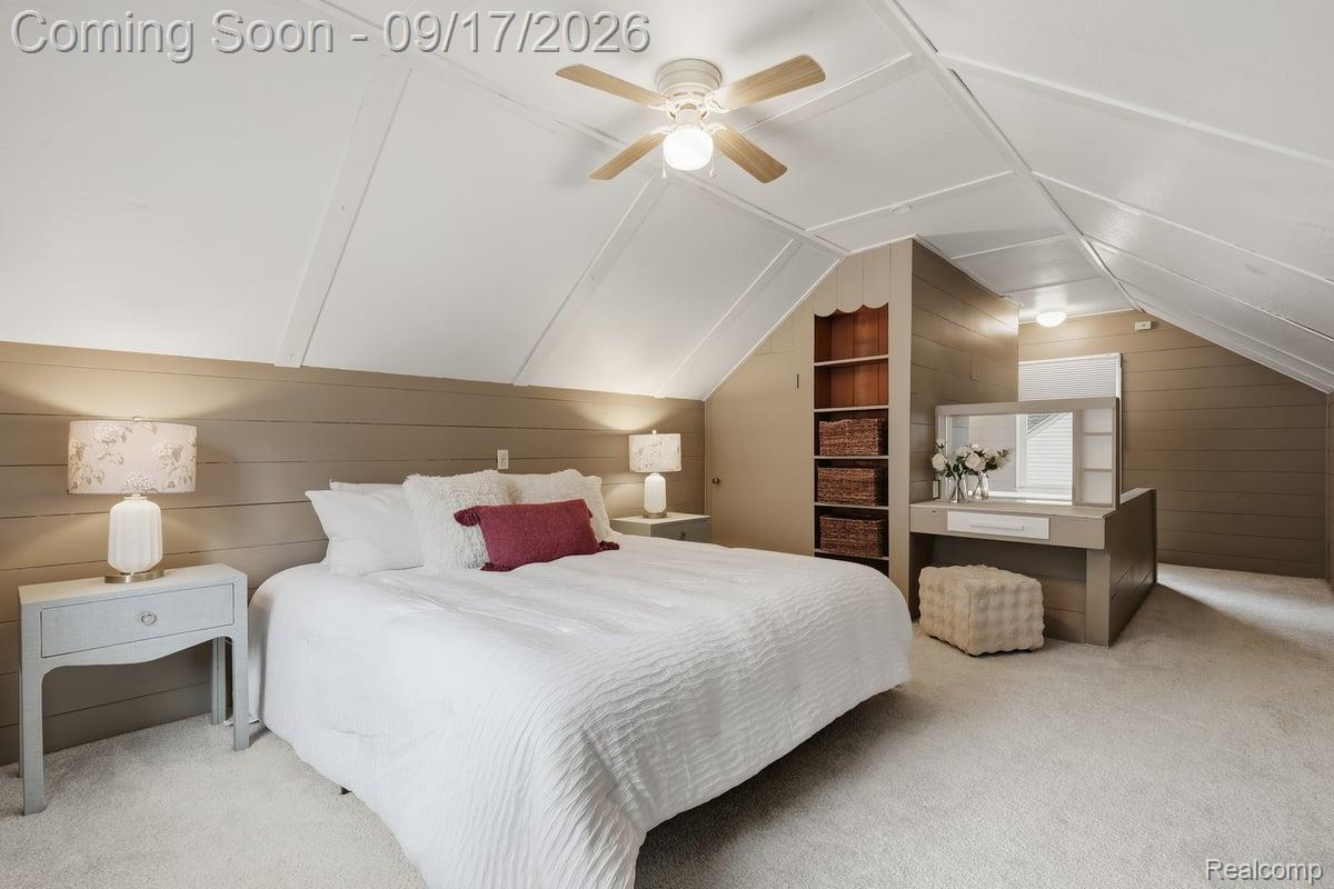 Attic bedroom with a white bed, sloped ceiling, ceiling fan, built-in shelves and vanity.