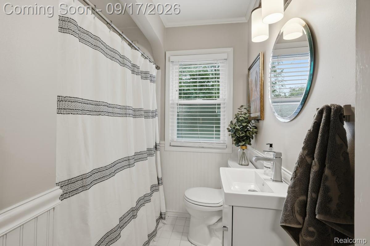 Bathroom with striped shower curtain, oval mirror, and white vanity beside a window.