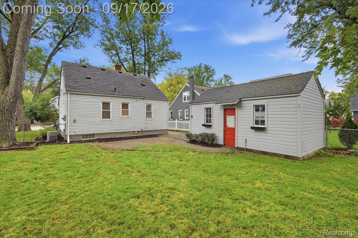 Rear exterior of a light-sided home and detached outbuilding with a red door and grassy yard.