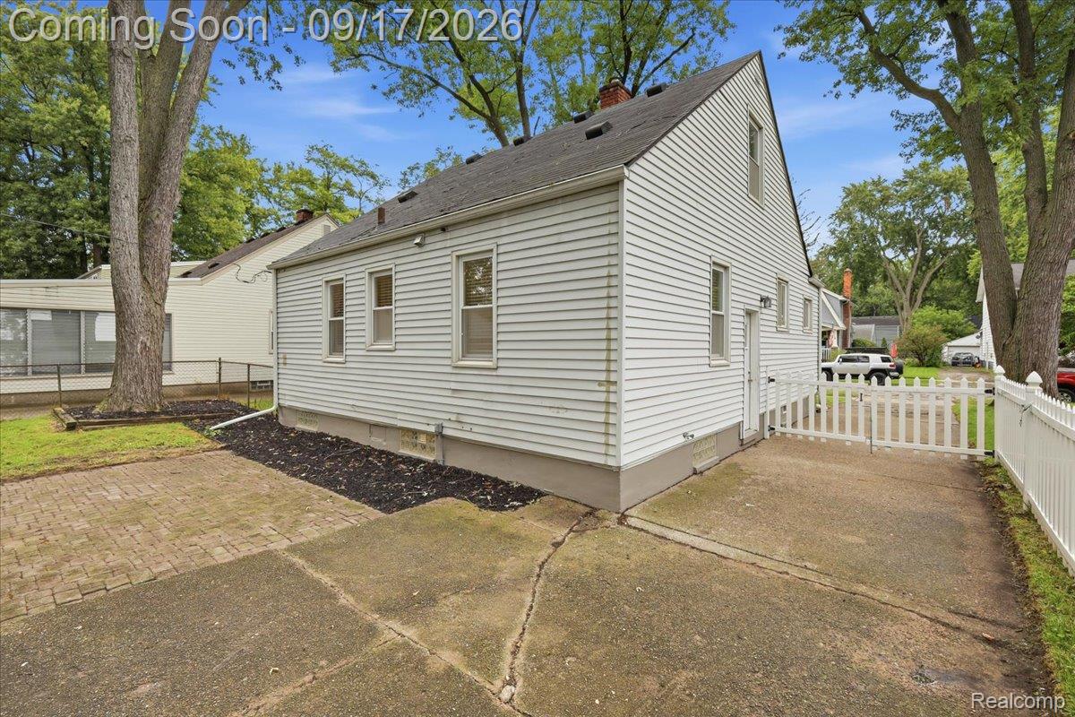 White-sided house with a steep gabled roof, paved driveway, and white picket fence.