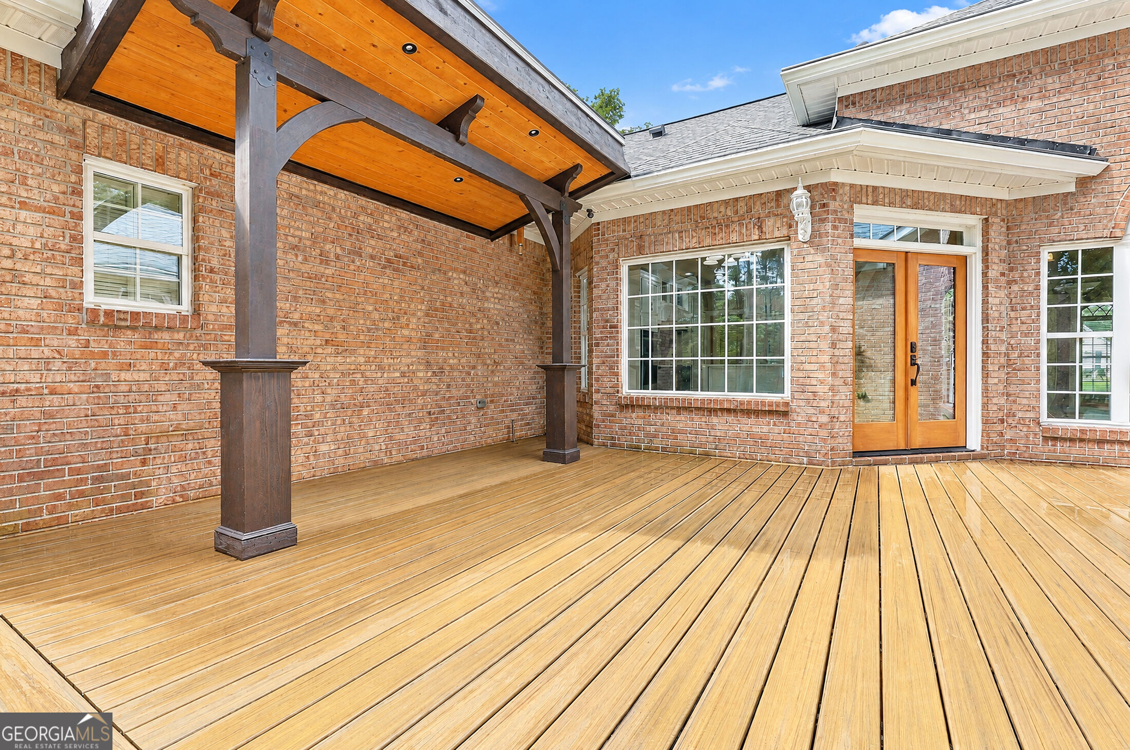 Brick house with a broad wooden deck beneath a timber-covered porch.
