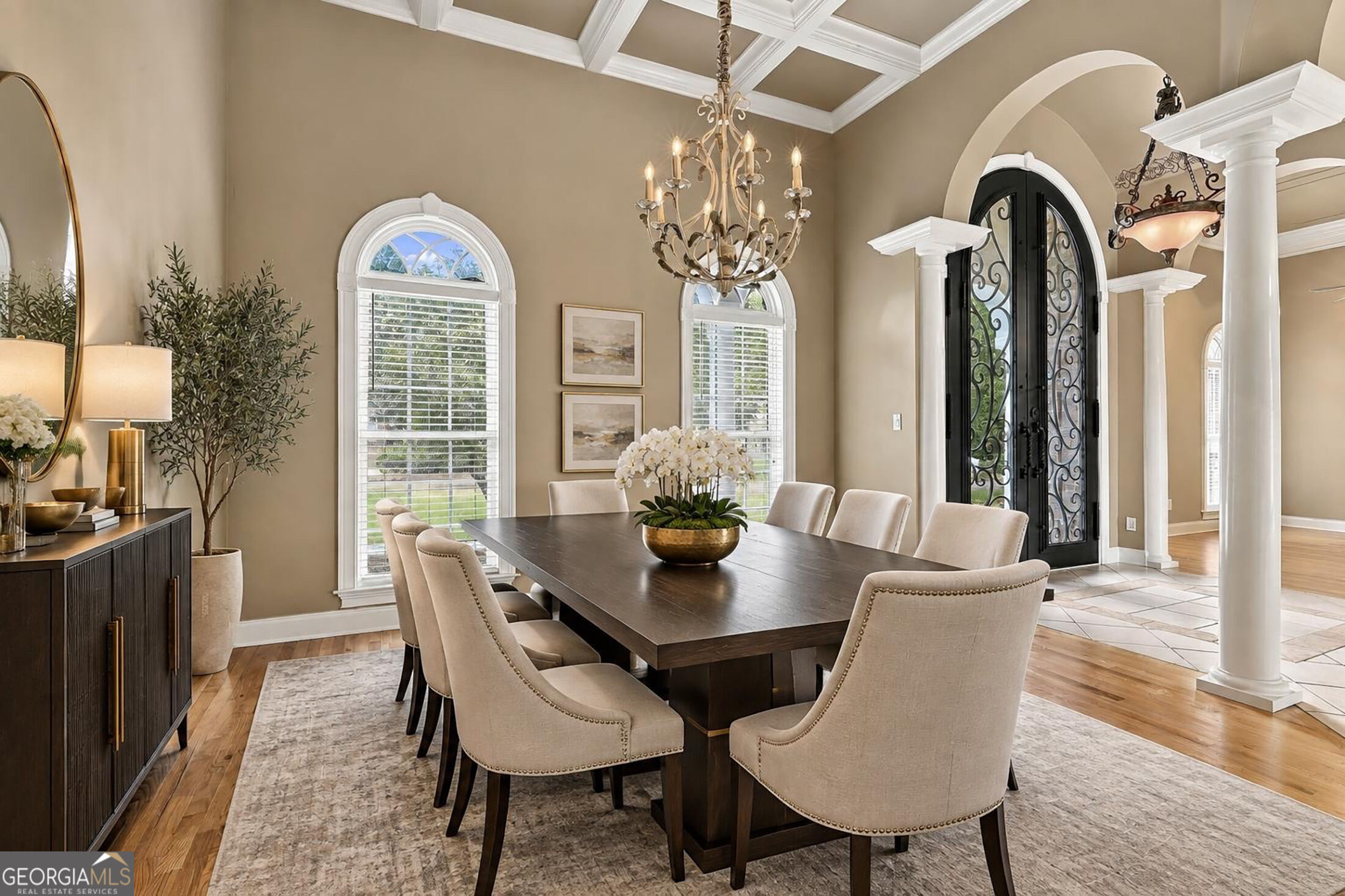 Dining room with a dark wood table, arched windows, coffered ceiling, and ornate black entry doors.