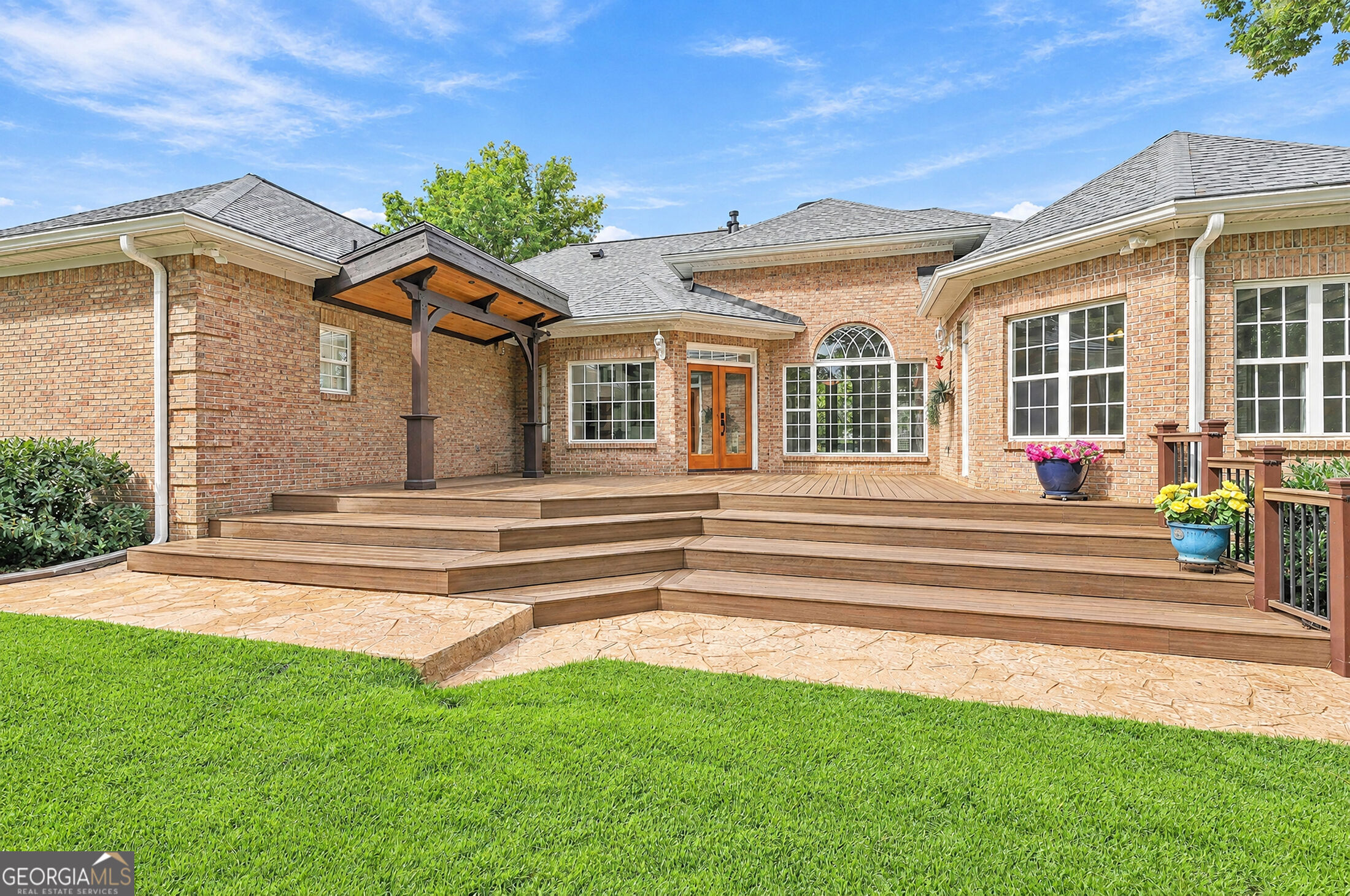 Brick home’s rear exterior with a multilevel deck, covered pergola, and stamped-stone patio.