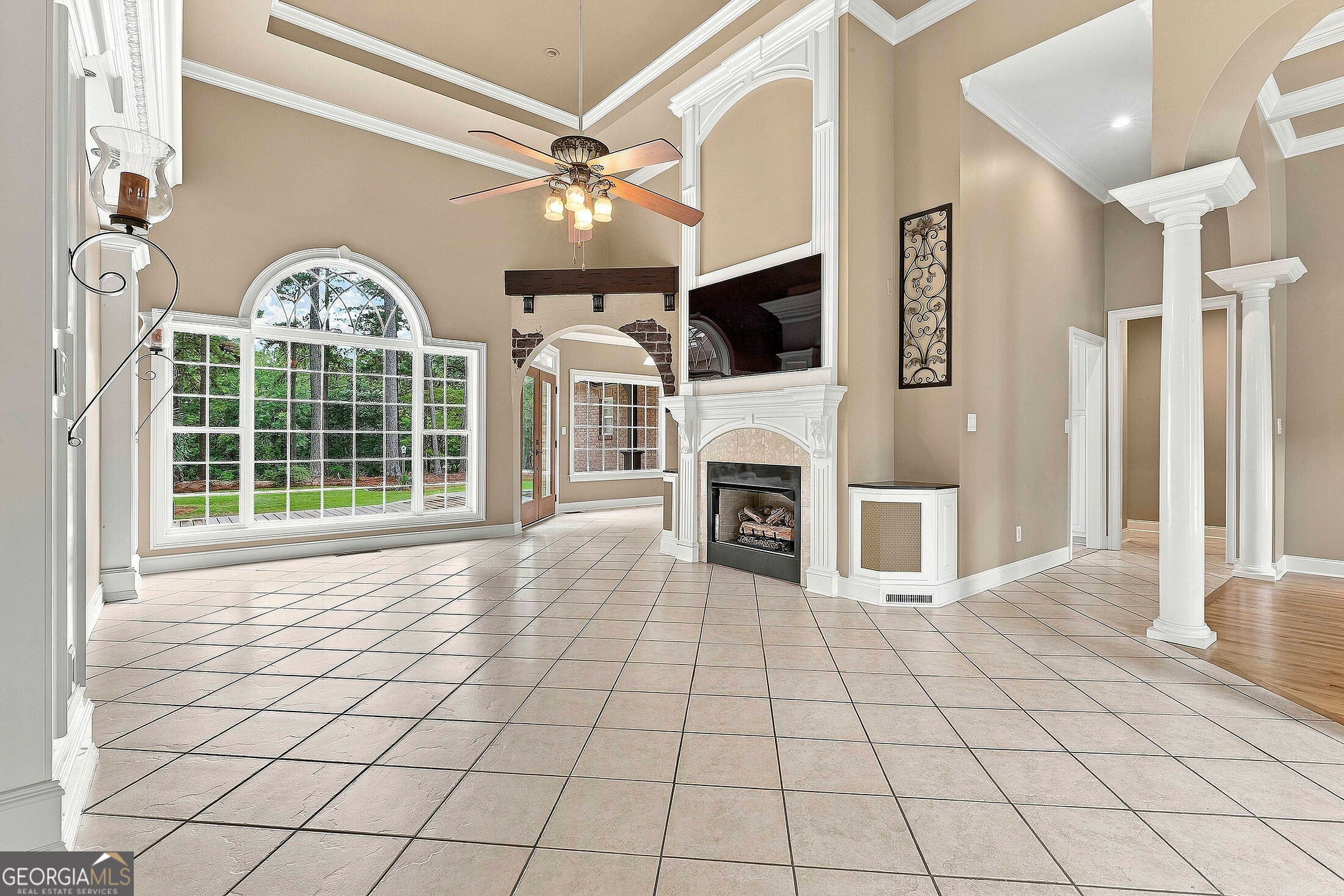 Unfurnished living room with an arched picture window, tiled floors, and a white-trimmed fireplace.