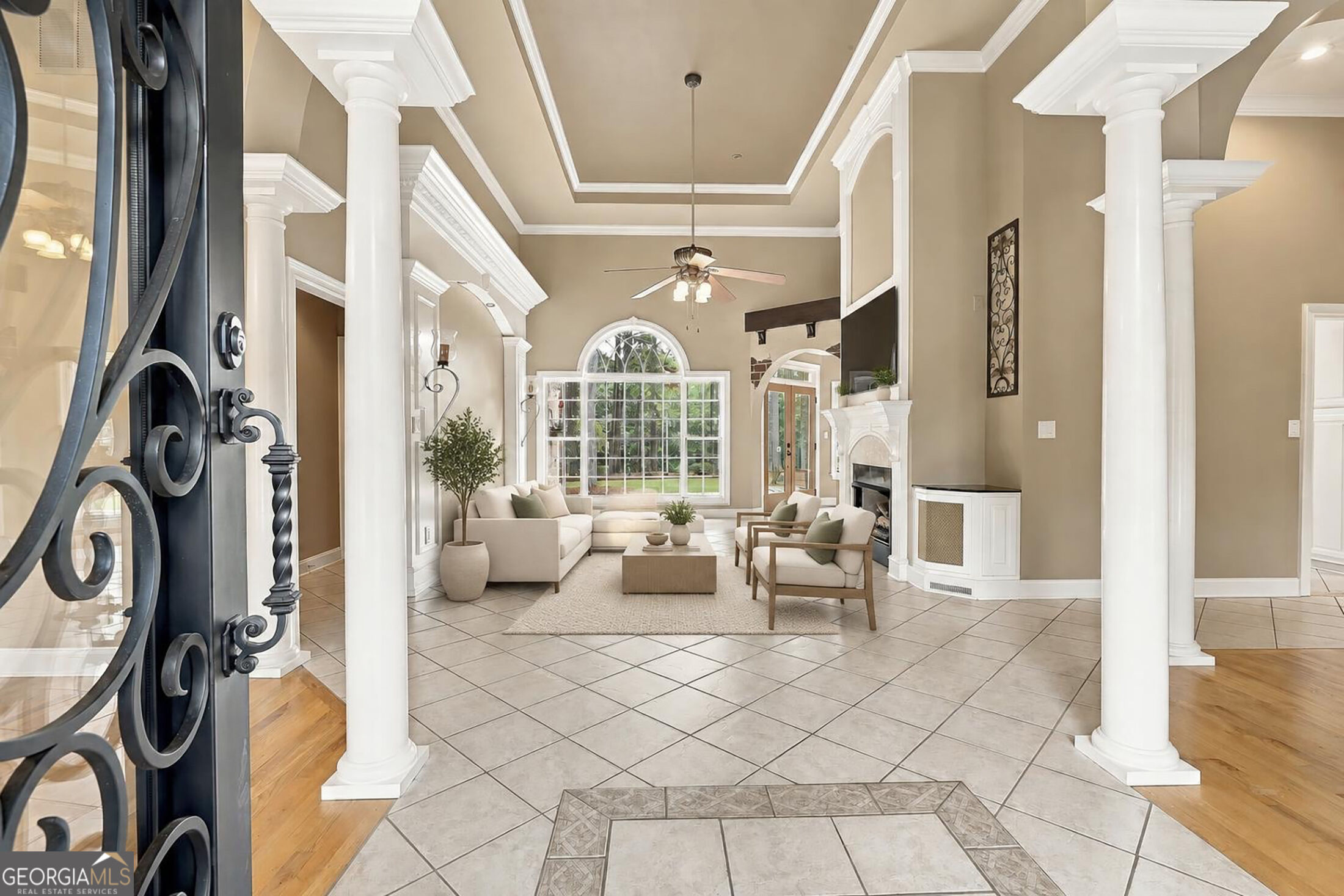 Living room with white columns, a fireplace, and a large arched window overlooking greenery.