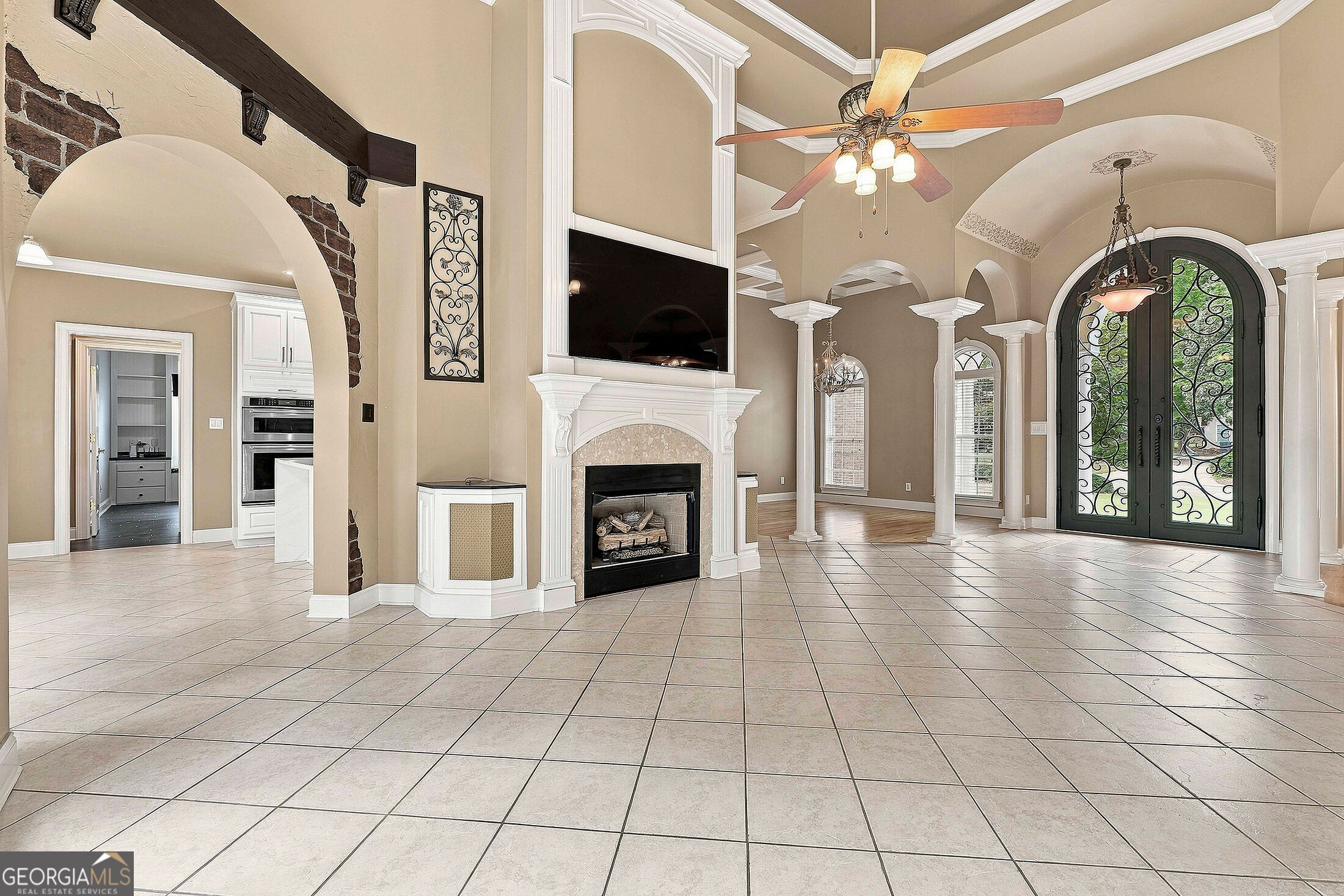 Vacant great room with a white fireplace, tiled floor, and arched wrought-iron entry doors.