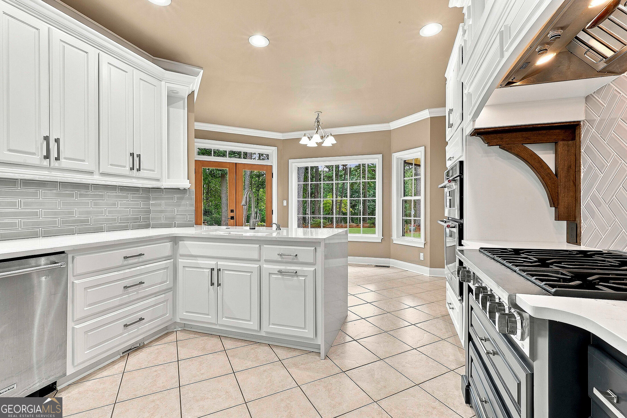 Kitchen with white cabinetry, gray tile backsplash, stainless steel appliances, and windows overlooking trees.