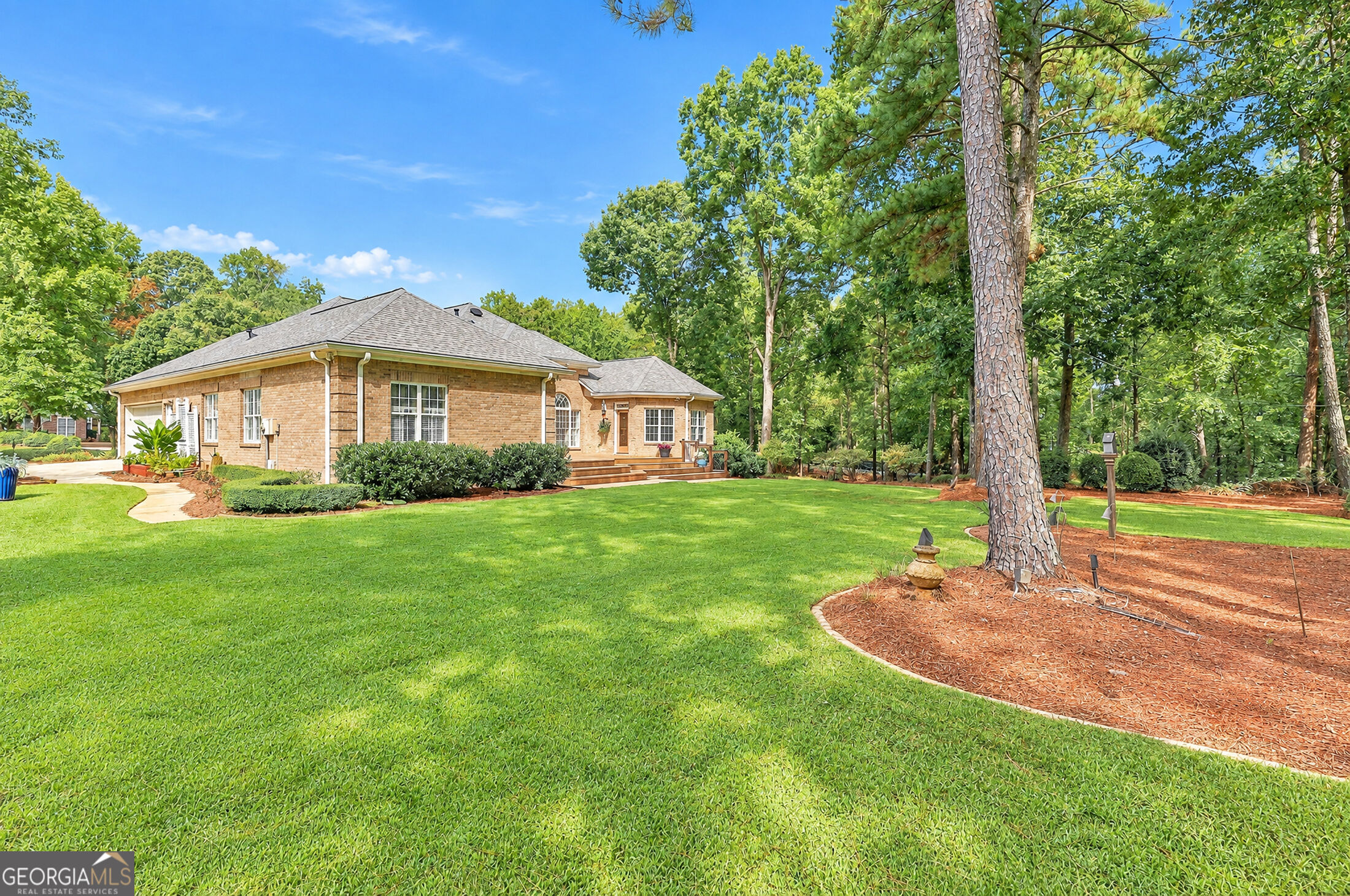Brick home with a raised deck, broad green lawn, and mature trees.