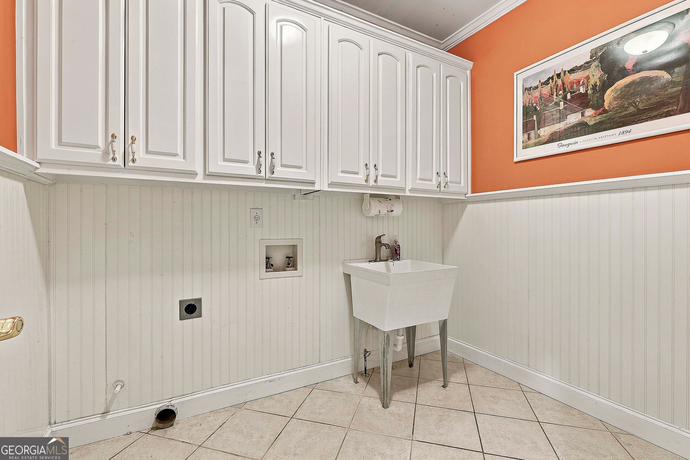 Laundry room with white cabinets, beadboard walls, and a freestanding utility sink.
