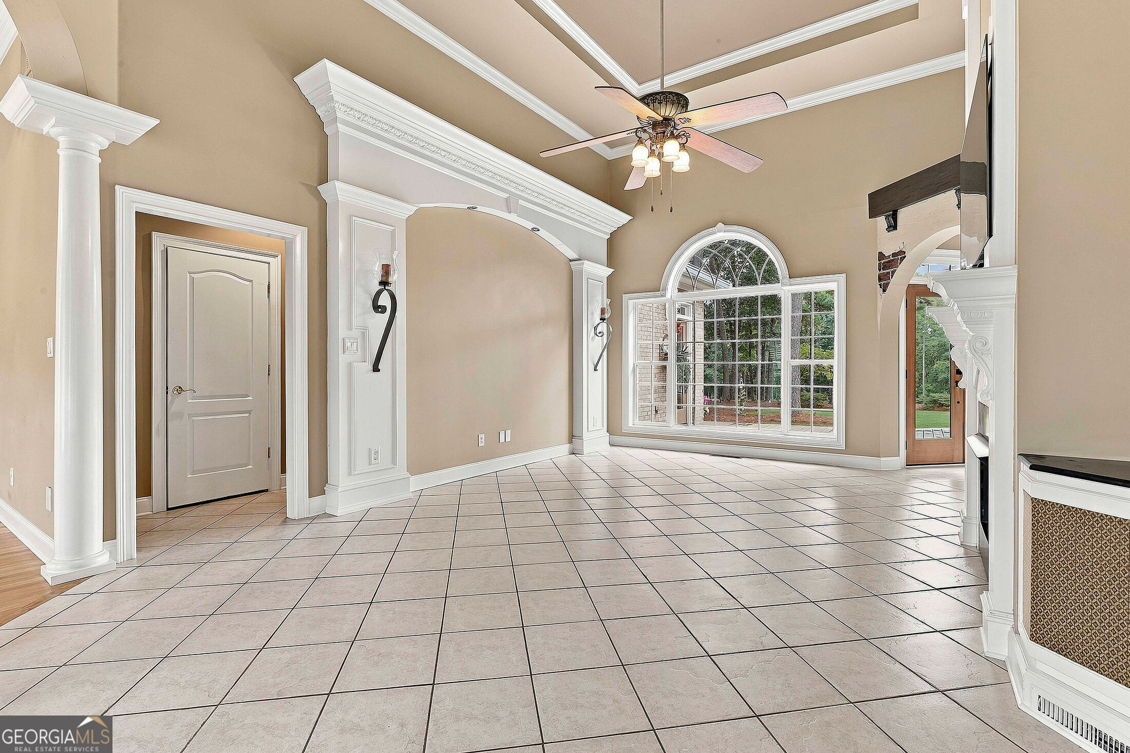 Empty room with a large tiled floor, ornate white columns, ceiling fan, and arched window.