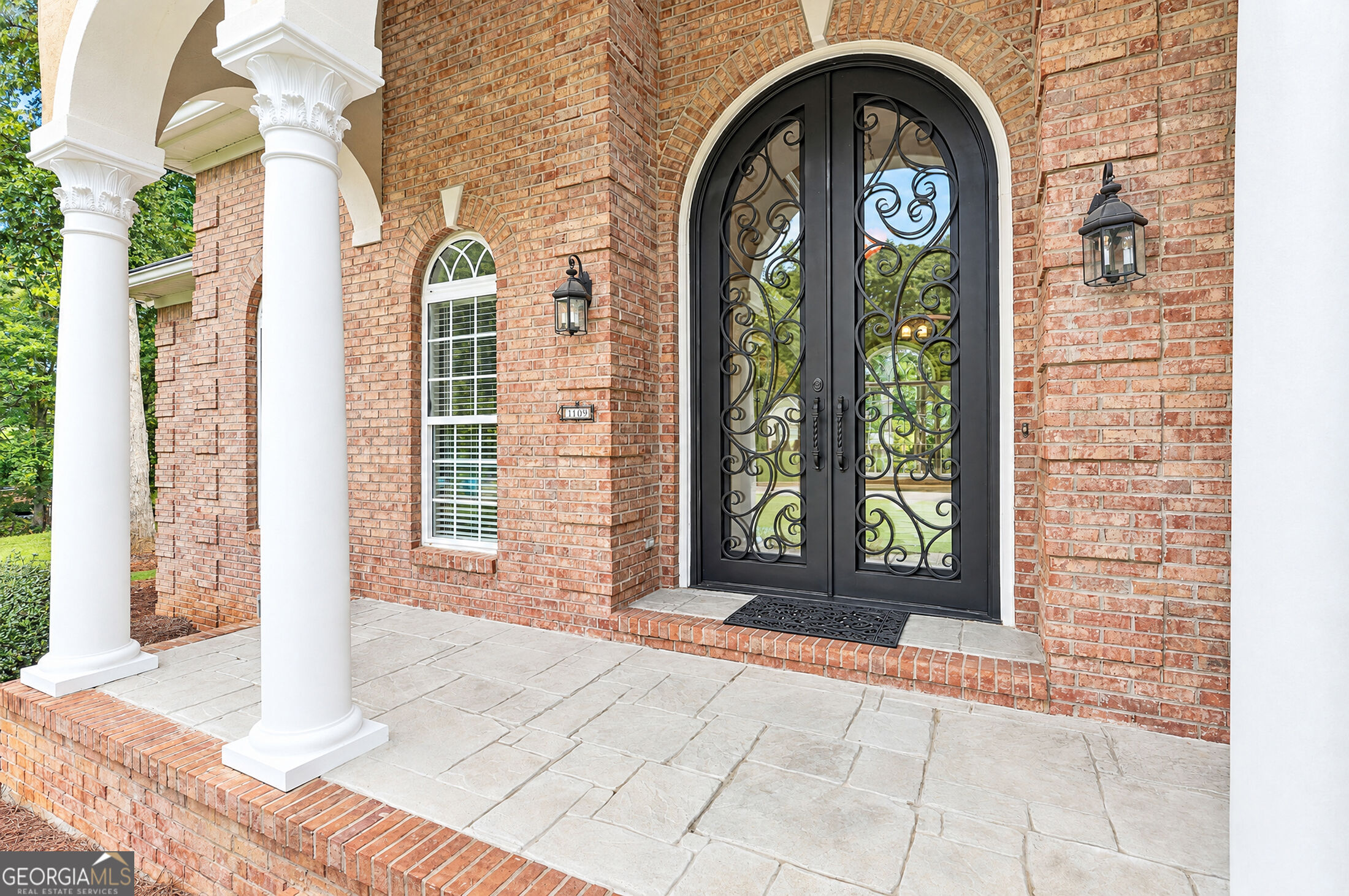 Brick home entry with ornate black double doors, white columns, and a stone porch.