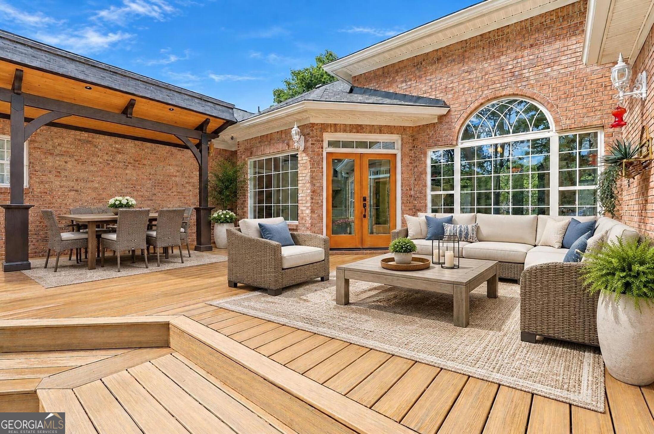 Wood deck with furnished lounge seating, covered dining area, and brick exterior.