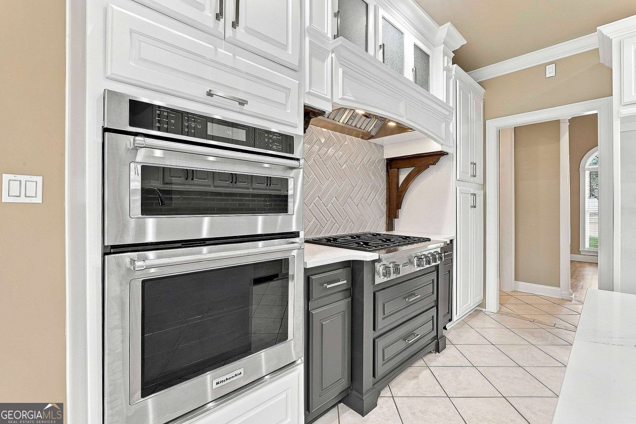 Kitchen with stainless double ovens, a gas range, gray cabinets, and a herringbone backsplash.