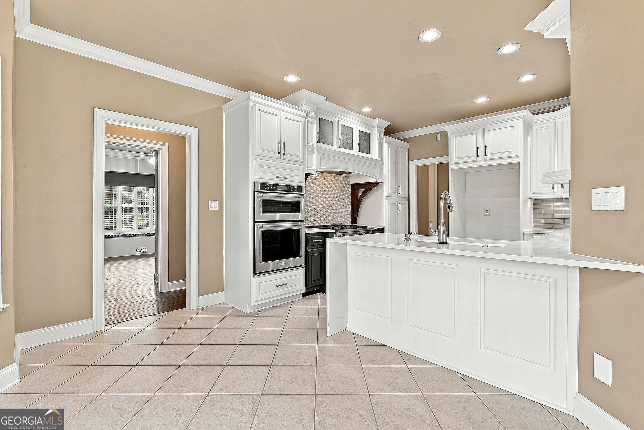 Kitchen with white cabinetry, a large island, stacked double ovens, and a herringbone backsplash.
